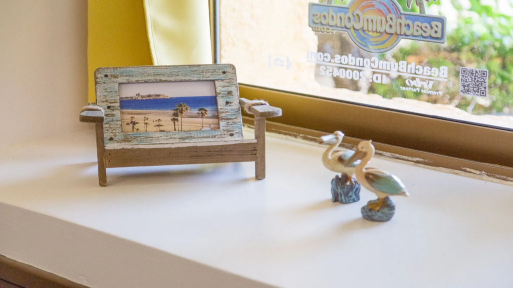 Coastal-themed decor with a beach photo and pelican figurines on a bright windowsill.