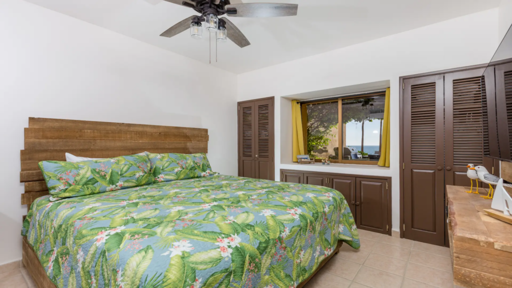 King-sized bed with tropical green palm leaf bedding and a rustic wood headboard.