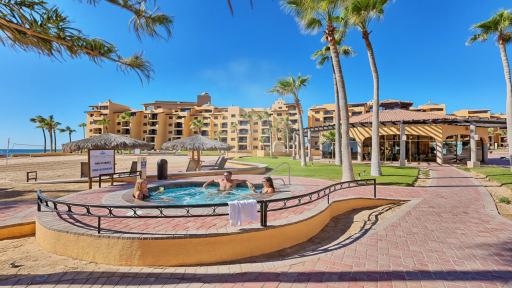 People enjoying a circular outdoor hot tub with a view of the beach and resort buildings in Penasco.