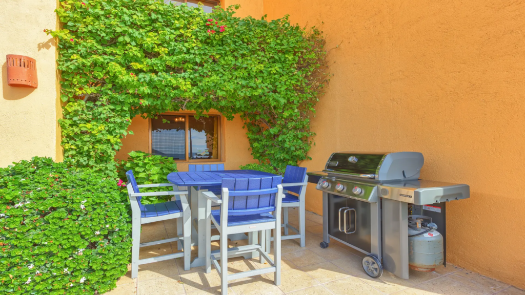 Close-up of a modern stainless steel grill and outdoor dining set surrounded by lush green vines.