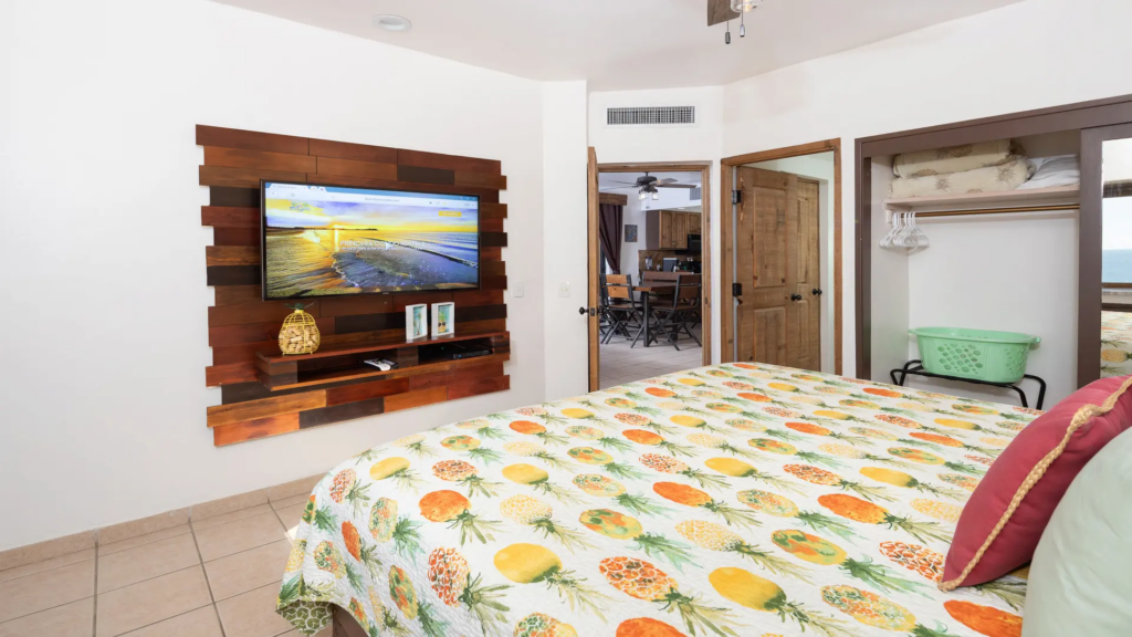 A cozy bedroom featuring a tropical pineapple print bedspread and a wall-mounted TV on a rustic wood panel.