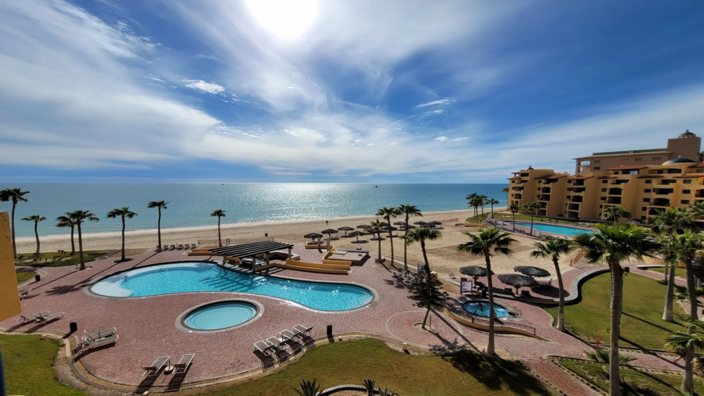High-angle view of multiple blue resort pools and palm trees along the Penasco coastline.