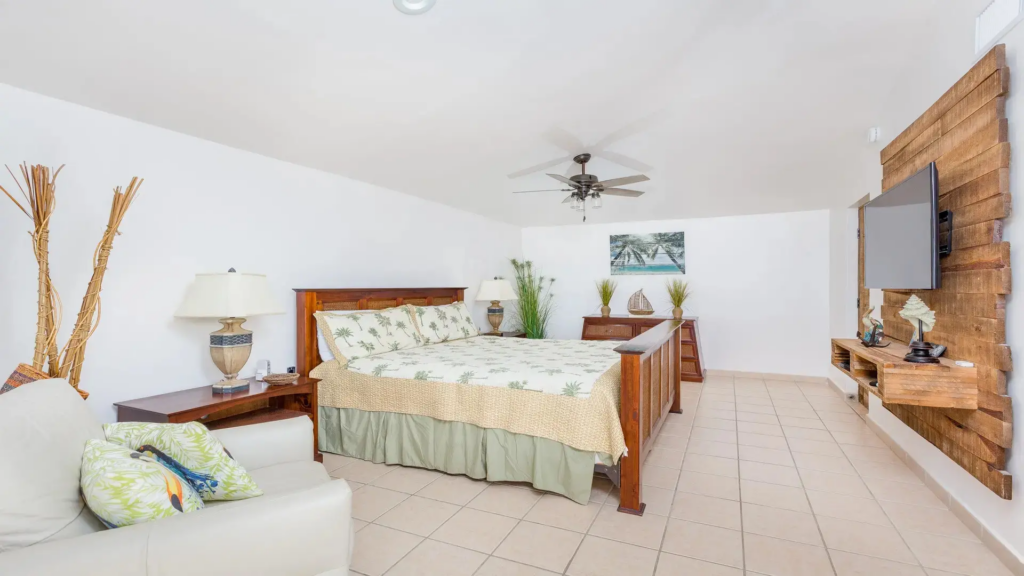 Wide-angle view of a large bedroom with tile flooring, a sitting chair, and rustic wood finishes.