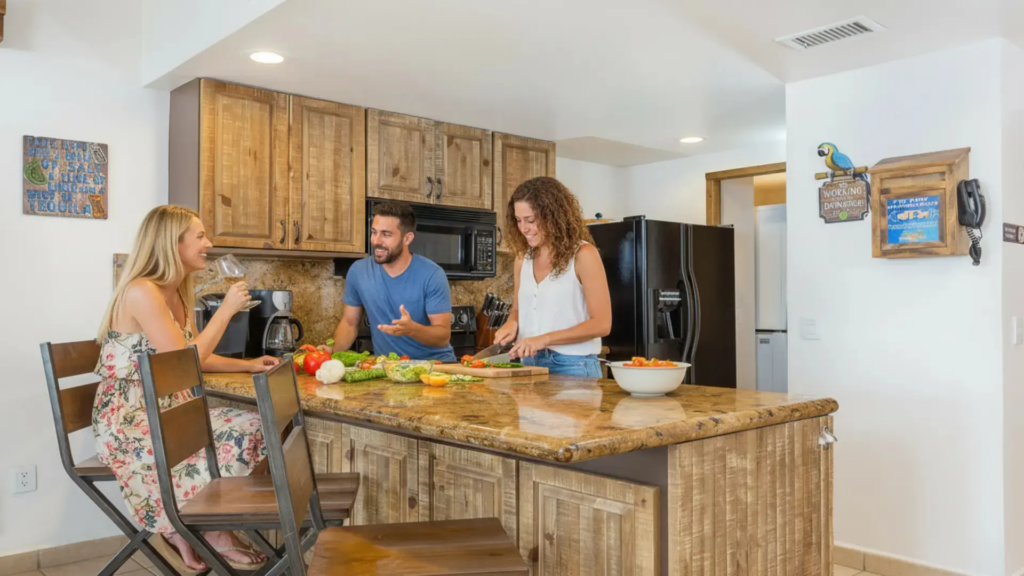 Three people laughing and preparing a healthy meal at a granite breakfast bar.