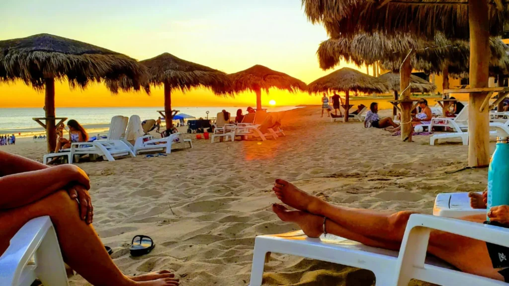 Sunset on Sandy Beach at Princesa Resort in Rocky Point, featuring palapas, lounge chairs, and guests relaxing by the ocean.1